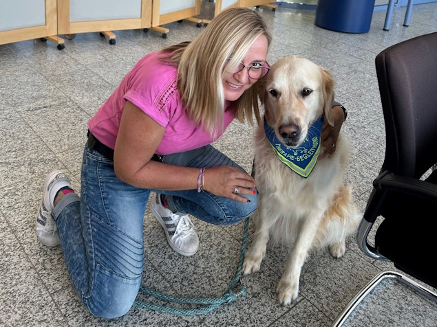 Tiertherapeutin Melanie Montag kniet neben Therapiehund Stitch.